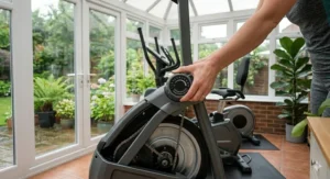 A photorealistic close-up illustration showing a user's hand adjusting the manual magnetic resistance dial on a 2 in 1 cross trainer and exercise bike.